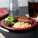 A white Creative Converting San Francisco 49ers paper dinner plate with broccoli, sausage, and macaroni on it on a table.