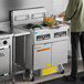 A man cooking food in a commercial kitchen using a Frymaster gas fryer.