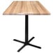 A Holland Bar Stool natural wood square bar height table with a black cross base.