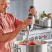 A man using a KitchenAid 300 Series immersion blender to blend food in a metal bowl.