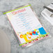 A Menu Solutions Alumitique menu board with green bands on a table with a white plate, a knife, and a fork.