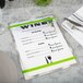 An Alumitique menu board with green bands on a table with a white plate, a knife, and a fork.