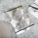 A Menu Solutions Alumitique menu board with black bands on a metal table with silverware.