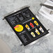 A Menu Solutions Alumitique aluminum menu board with black bands on a table with a knife and fork.
