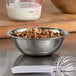 A Vollrath stainless steel mixing bowl filled with walnuts on a table.