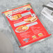 A customizable Alumitique swirl aluminum menu board with red bands on a table with a menu, silverware, and a white napkin.