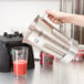 A person using a Waring commercial blender to make a strawberry smoothie.