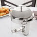 A Libbey stainless steel chafing dish with a lid on a white surface.