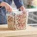 A person holding a Choice clear square polycarbonate food storage container of beans.