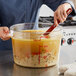 A person stirring a large clear round container of food.