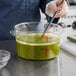 A person measuring green liquid in a clear Choice food storage container.