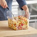 A person cutting up food in a Choice square food storage container.