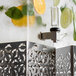 A Rosseto clear acrylic rectangle beverage dispenser with a metal container of cucumber and lemon slices.