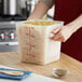 A person holding a Choice translucent square polypropylene container of pasta.