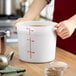 A person holding a large white Choice food storage container with red liquid in it.