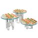 A group of small round glass tables with food on a Rosseto clear tempered glass riser shelf.