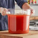 A man holding a Choice clear polycarbonate food storage container filled with red liquid.