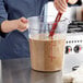 A person stirring a liquid in a Choice clear round food storage container.