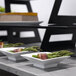 A table with white square Rosseto bowls filled with green asparagus wrapped in bacon.