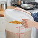 A person's hand holding a Choice translucent plastic food storage container filled with pasta.
