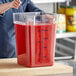 A woman stirring red liquid in a Choice clear polycarbonate food storage container.