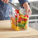 A person cutting vegetables in a Choice clear square polycarbonate food storage container.