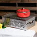 A red pot with a lid on a metal grill over a metal container.