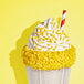 A milkshake topped with whipped cream and yellow sprinkles, served with a red and white striped straw.