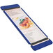 A blue Menu Solutions wood menu board with rubber band straps on a table with a menu showing a picture of spaghetti.