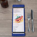 A Menu Solutions True Blue wood menu board with rubber band straps on a table with a fork and knife.