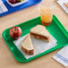 A green plastic fast food tray holding a peanut butter and jelly sandwich, an apple, and a cup of iced beverage.