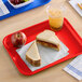 A red plastic fast food tray holding a sandwich, an apple, and a cup of iced beverage.
