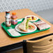 A green plastic fast food tray with a sandwich, fruit, and a bottle of juice on a table.