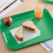 A green plastic fast food tray holding a peanut butter and jelly sandwich, an apple, and a cup of iced drink.