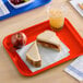 A rectangular orange plastic fast food tray holding a sandwich, an apple, and a cup of iced beverage.