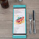 A Sky Blue wood menu board on a table in an Italian restaurant with pasta and basil on it.