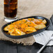 A plate of fries with cheese and herbs next to a glass of soda on a table with a napkin and a fork.