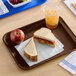 A chocolate brown plastic fast food tray holding a peanut butter and jelly sandwich, an apple, and a cup of iced drink.