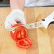 A person in gloves uses a Mercer Culinary Millennia utility knife to cut a tomato on a counter.