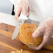 A person in gloves cutting a loaf of bread with a Mercer Culinary Millennia utility knife.