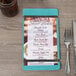 A customizable wood menu board with rubber band straps on a table with silverware and a menu.