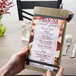 A hand holding a Menu Solutions weathered walnut wood menu board on a table.