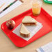 A red plastic fast food tray holding a peanut butter and jelly sandwich, an apple, and a cup of iced drink.