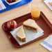 A burgundy plastic fast food tray holding a peanut butter and jelly sandwich, an apple, and a cup of iced beverage.