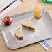 A gray plastic fast food tray holding a sandwich, an apple, and a cup of iced beverage.