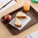A rectangular chocolate brown plastic fast food tray holding a sandwich, an apple, and a cup of iced drink.