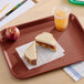 A rectangular burgundy plastic fast food tray holding a sandwich, an apple, and a cup of iced beverage.