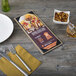 A customizable wood menu board with top and bottom strips on a table with a menu, fork, and knife.