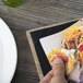 A person holding a Menu Solutions wood menu board over a plate of food.