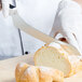 A person wearing white gloves uses a Mercer Culinary Millennia bread knife to cut a loaf of bread.